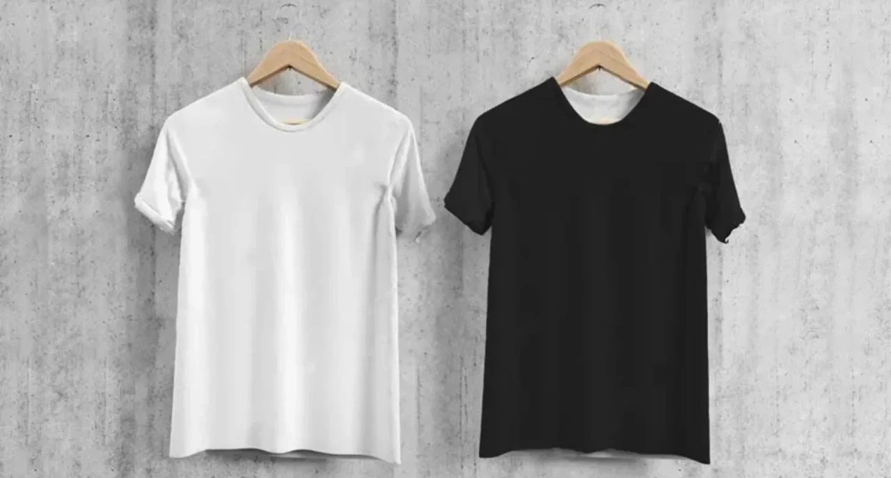 コンクリートの壁を背景に白と黒のTシャツが並んでハンガーにかけられている。